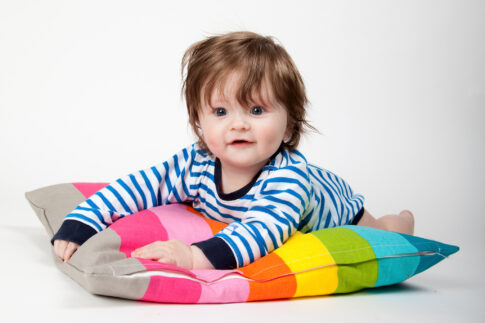Baby sitting against a white background with a colourful cushion