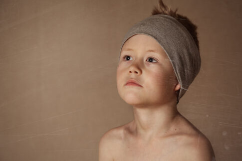 Portrait of a young boy wearing a grey headband against a warm brown background
