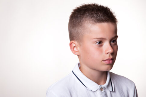 Portrait of a young boy wearing a white polo shirt against a light background