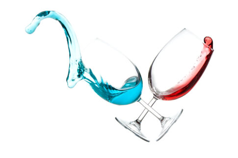 Two glass vessels with blue and red liquid splashing between them