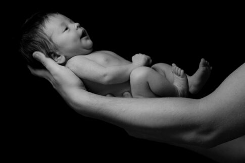 Black and white photograph of a newborn baby resting in an adult's hands