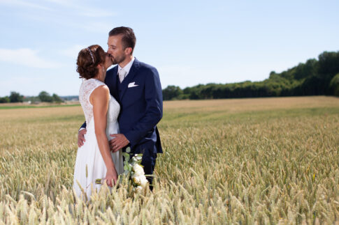 Bride and groom standing together in a sunlit wheat field
